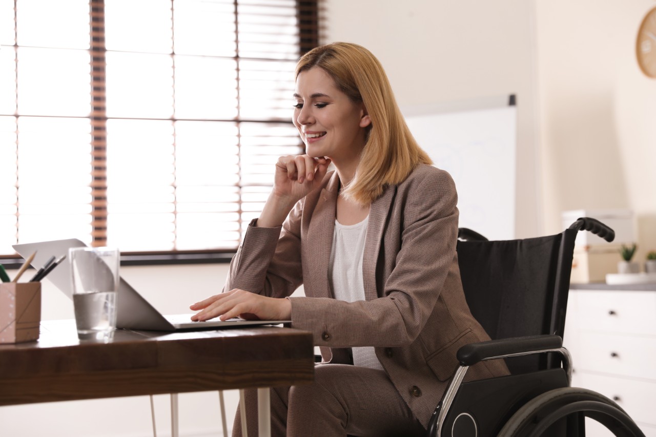 Portrait of woman in wheelchair working with laptop at table indoors
